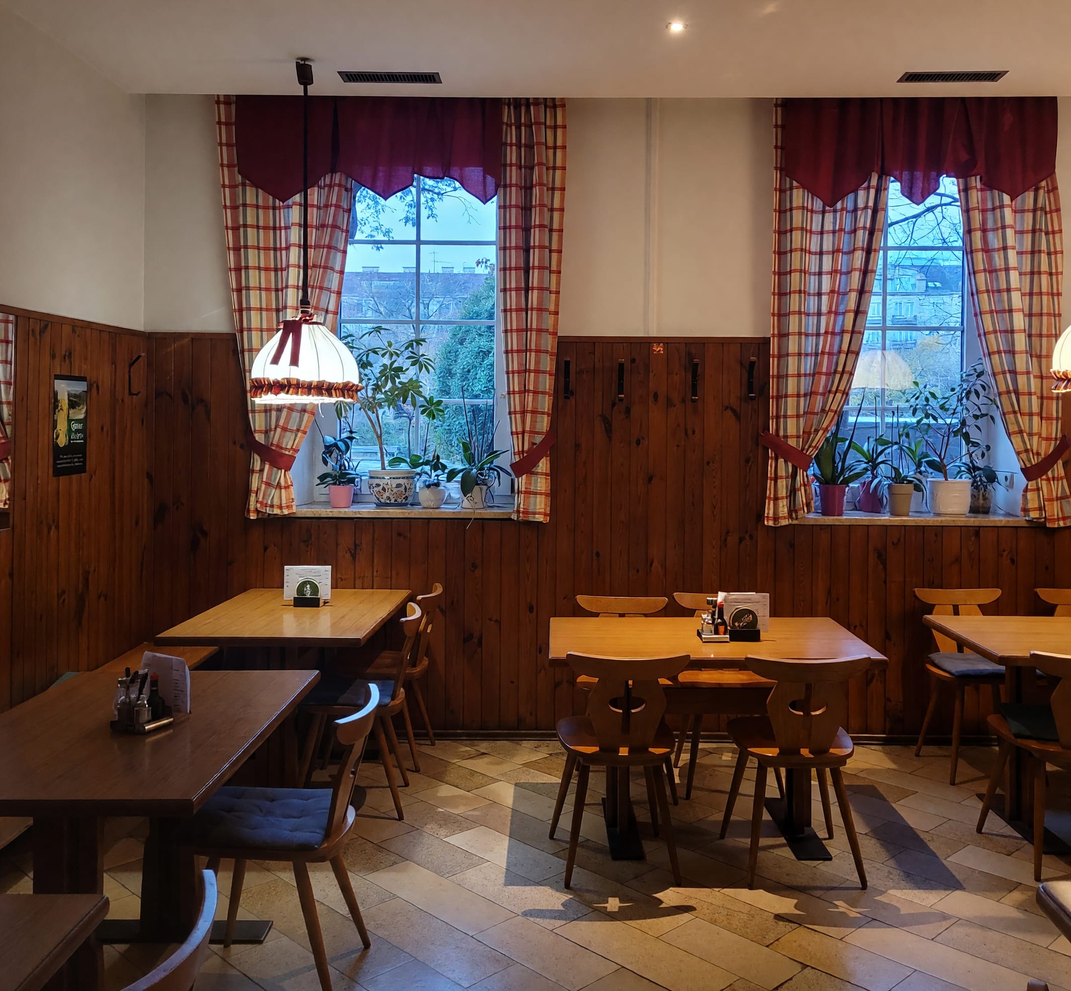 Gaststube im Gasthaus Hold: dunkle Holzvertäfelung, rot-weiß karierte Vorhänge und Holztische vor zwei Fenstern