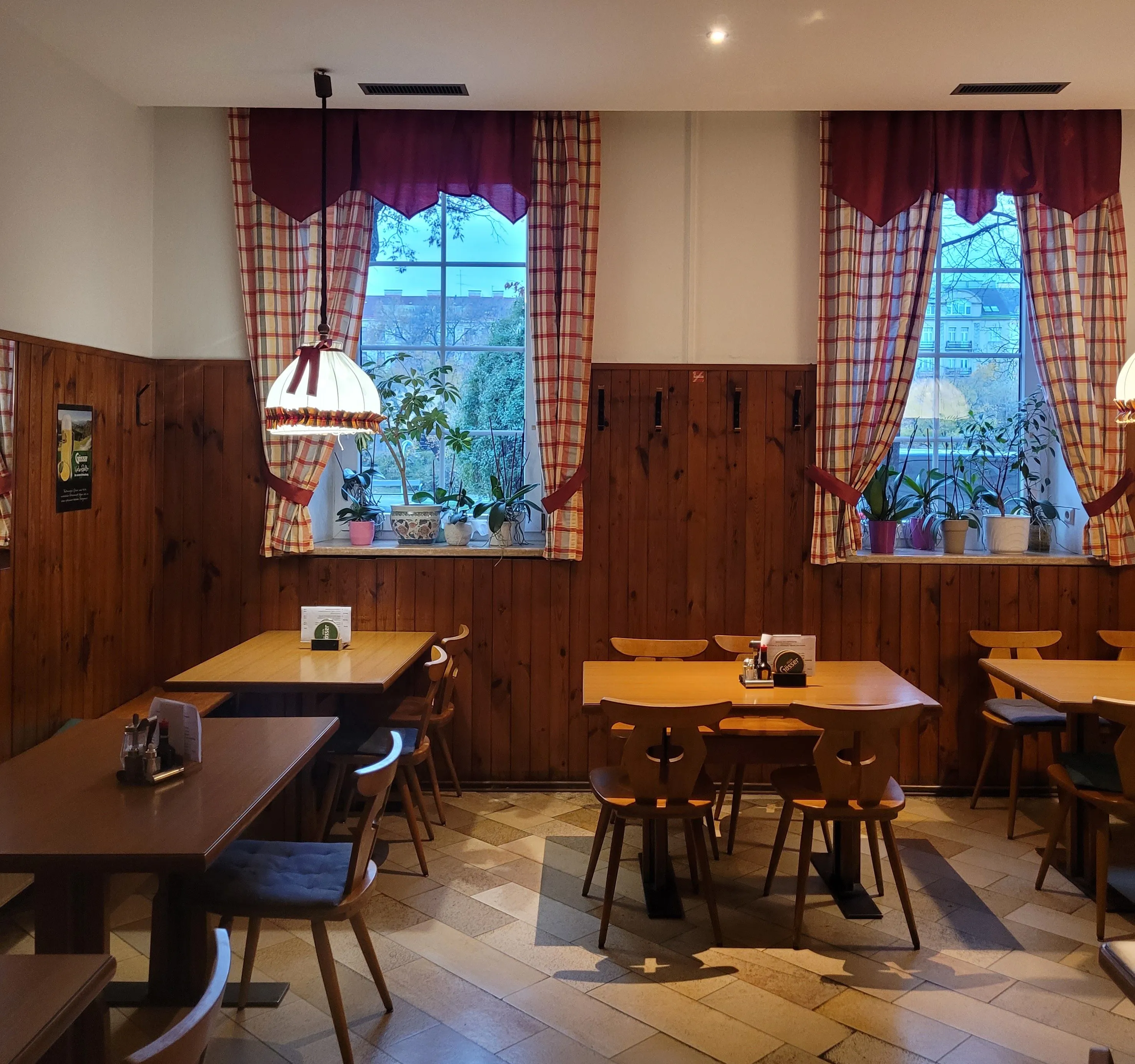 Gaststube im Gasthaus Hold: dunkle Holzvertäfelung, rot-weiß karierte Vorhänge und Holztische vor zwei Fenstern