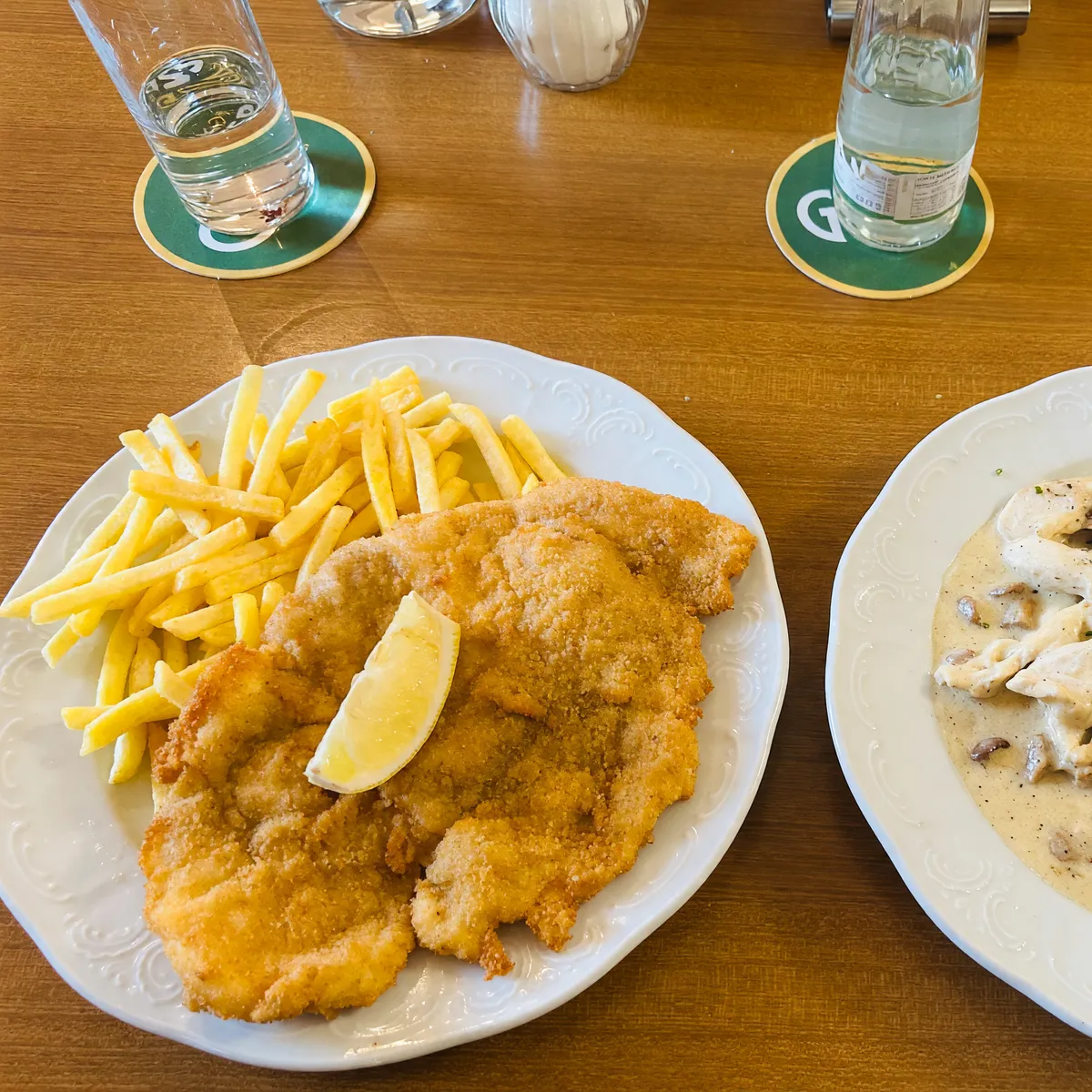Schnitzel mit Pommes frites auf einem Holztisch, daneben Gläser auf Bierdeckeln