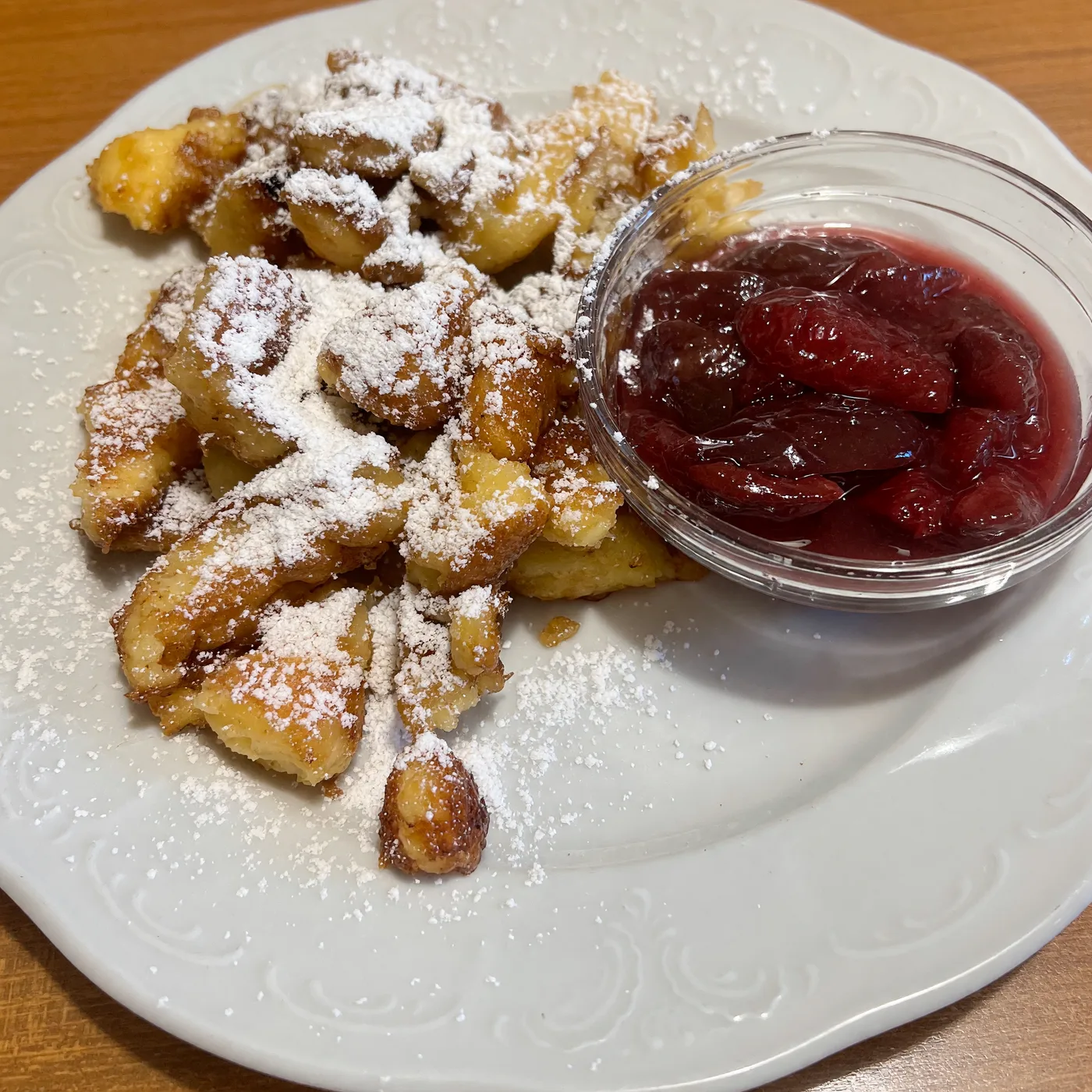 Kaiserschmarrn mit Staubzucker, daneben ein Glasschälchen Röster, auf einem weißen Teller