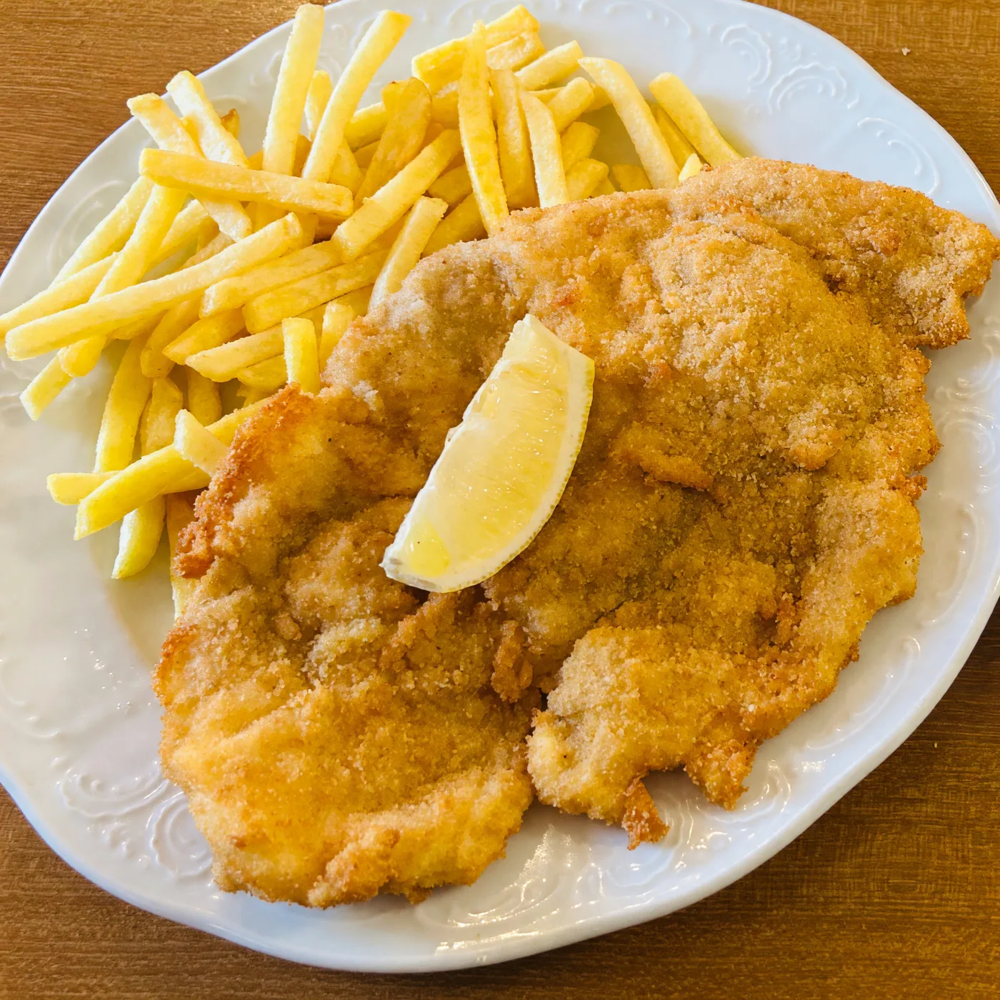 Schnitzel mit Pommes frites und einer Zitronenspalte auf einem weißen Teller, fotografiert von einem Gast
